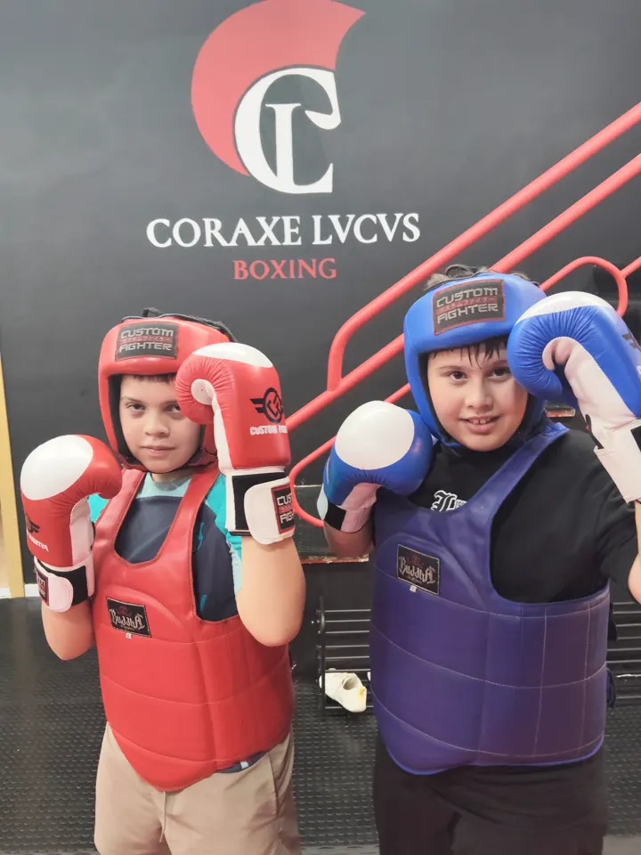 Dos chavales con casco, peto y guantes delante del logo de Coraxe Lvcvs